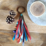 Porte-clefs Ciewenn composé d’un pompon, fait main, avec des rubans et des suédines bleues, oranges, rouges, décoré de perles et de chaînettes.
