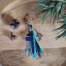 Porte-clefs Ciewenn composé de perles, d’une pampille, d’un pompon, fait main, avec rubans, suédines, de ton argenté et camaïeu de bleu et vert,
